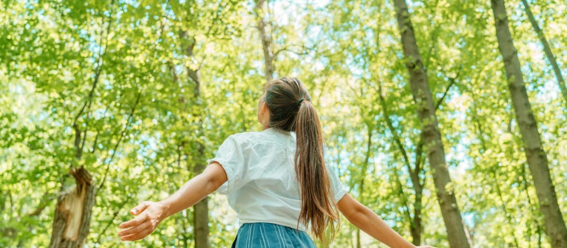 Free woman breathing clean air in nature forest. Happy girl from the back with open arms in happiness. Fresh outdoor woods, wellness healthy lifestyle concept. חרדת בחינות